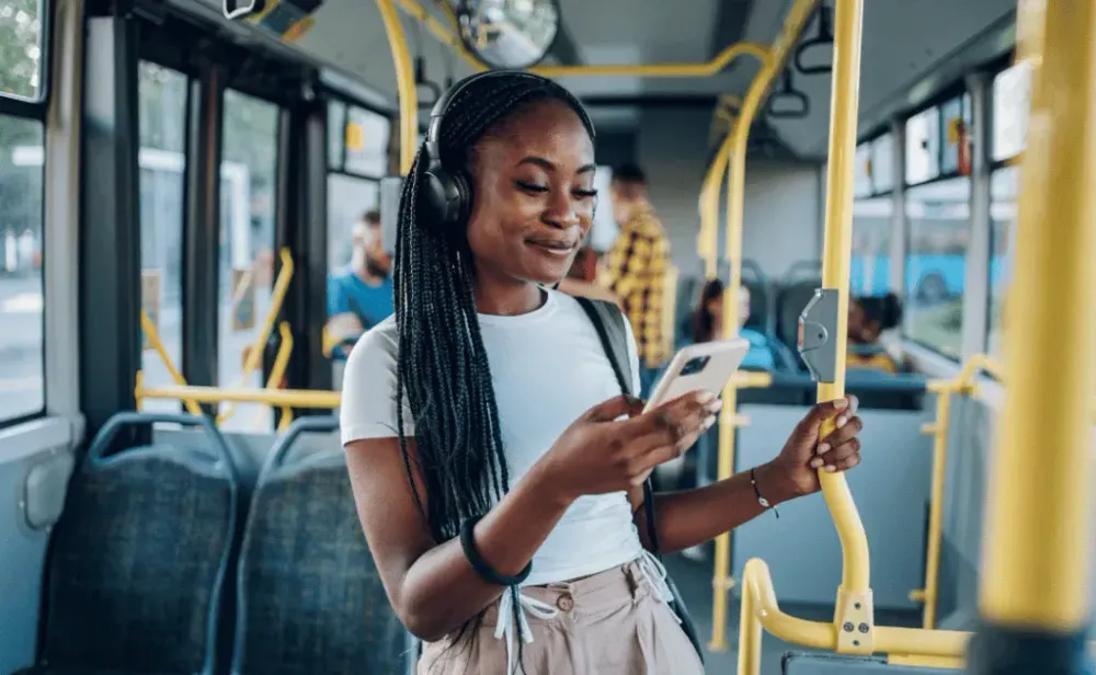 Black woman using smartphone and listening to headphones while riding a bus
